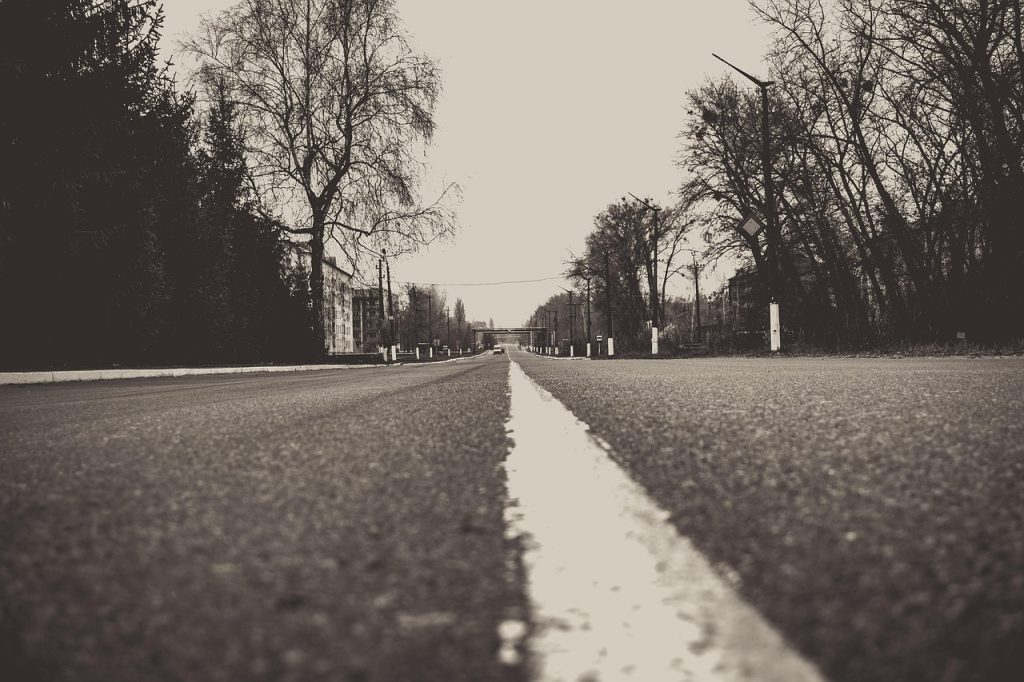 Monochrome image depicting a long, straight road leading towards a distant school building, symbolizing