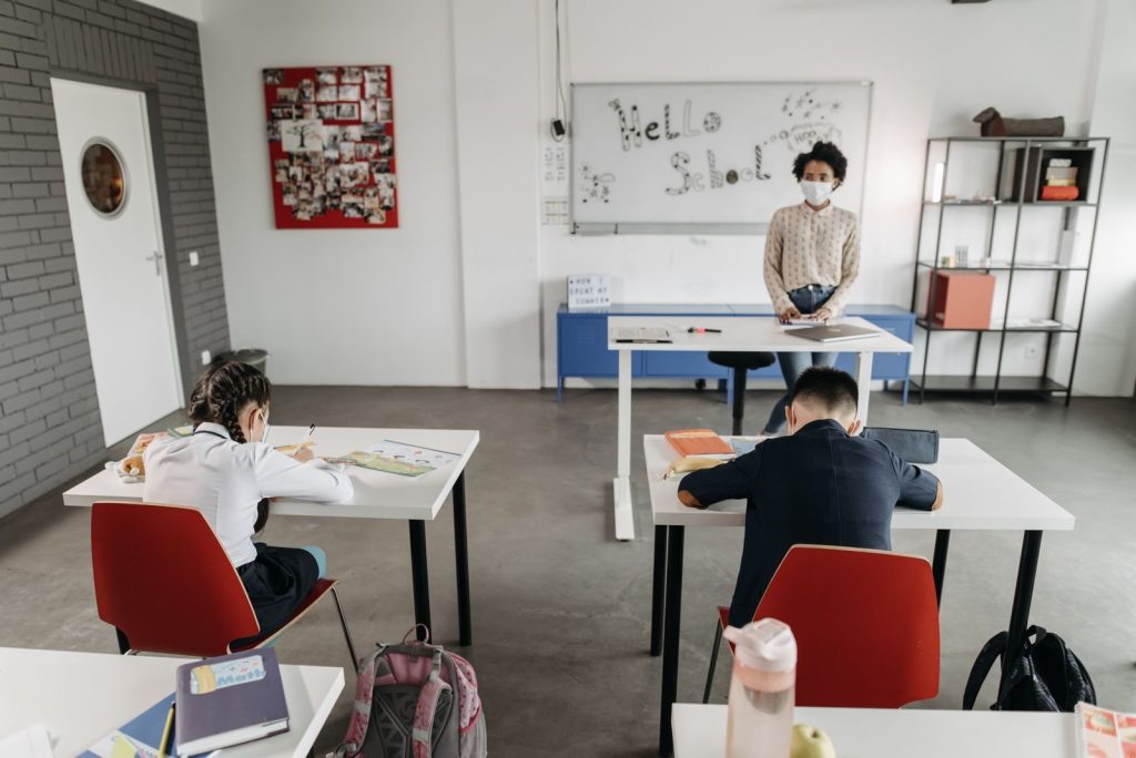 A classroom scene with children and a teacher wearing masks, a sign of new normal education.