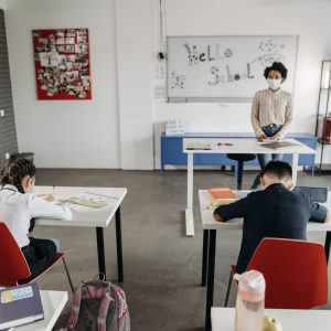 A classroom scene with children and a teacher wearing masks, a sign of new normal education.