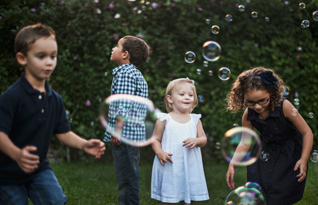 Four children playing with floating bubbles in a green garden